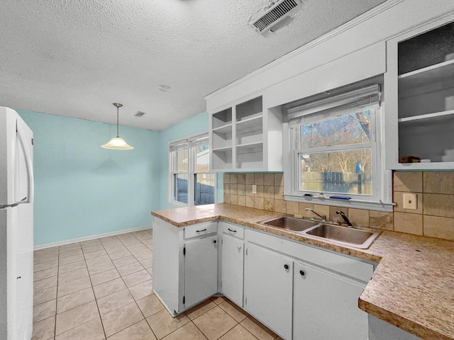 kitchen featuring open shelves, tasteful backsplash, visible vents, freestanding refrigerator, and a sink