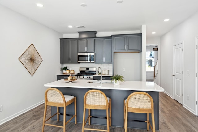 kitchen with dark hardwood / wood-style floors, sink, backsplash, stainless steel appliances, and a center island with sink