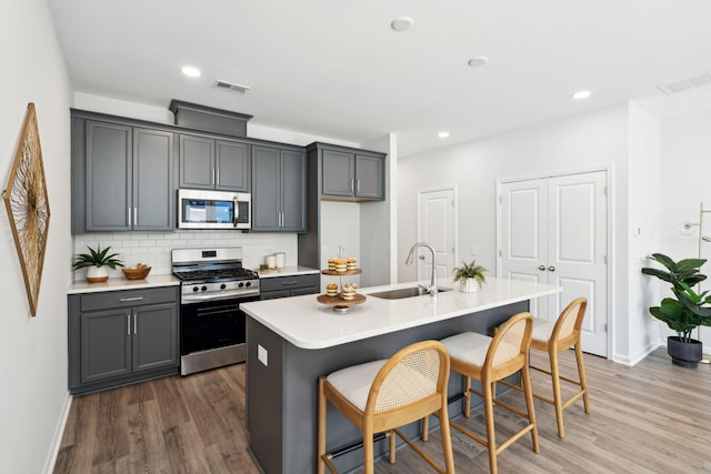 kitchen featuring sink, a kitchen island with sink, gray cabinetry, stainless steel appliances, and a kitchen bar