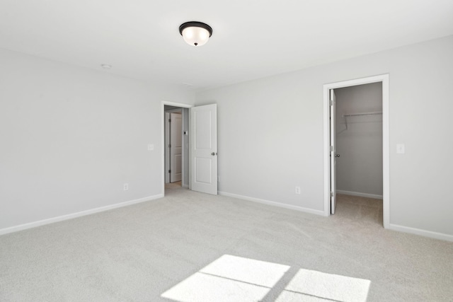 unfurnished bedroom with a walk in closet, a closet, and light carpet