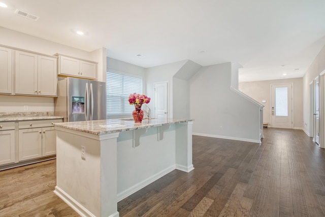 kitchen with a center island, dark hardwood / wood-style floors, stainless steel fridge, and light stone counters