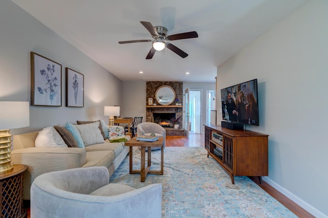 living area featuring a fireplace, a ceiling fan, baseboards, and wood finished floors