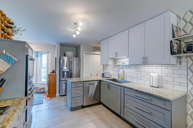 kitchen featuring decorative backsplash, gray cabinetry, stainless steel appliances, and a sink