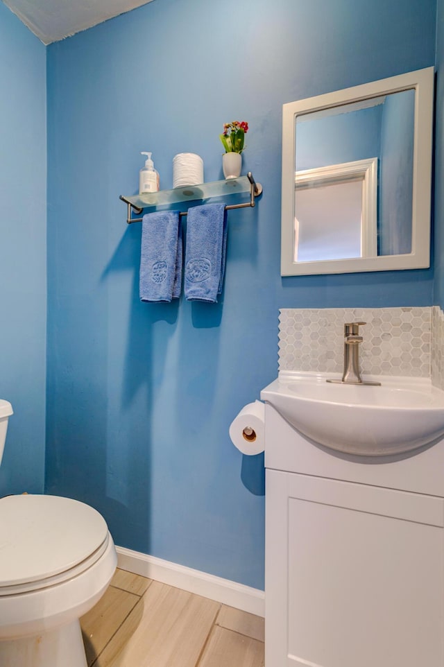 bathroom featuring vanity, wood finished floors, baseboards, decorative backsplash, and toilet