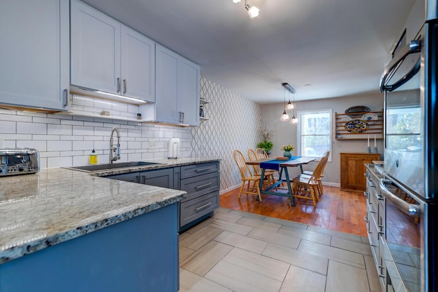 kitchen with pendant lighting, open shelves, a sink, decorative backsplash, and light stone countertops