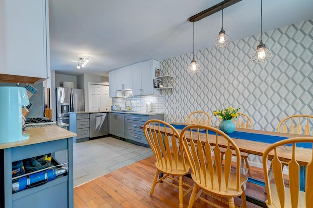 kitchen with light wood-style flooring, a sink, hanging light fixtures, light countertops, and appliances with stainless steel finishes