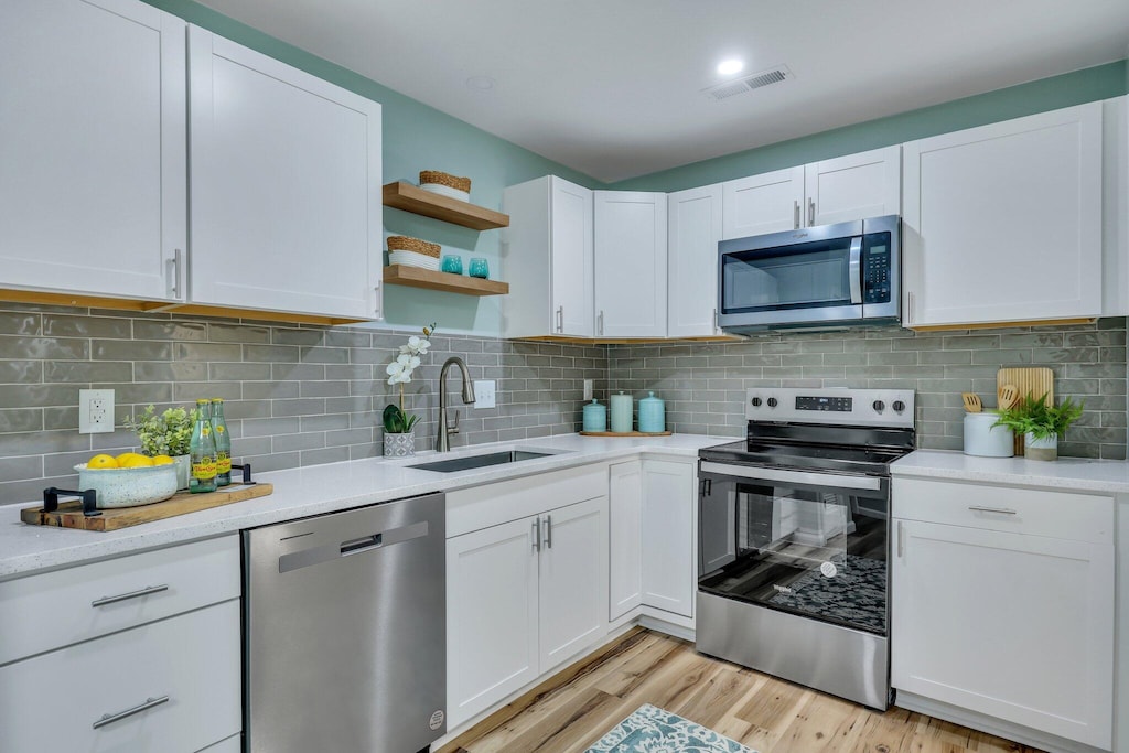 kitchen featuring white cabinets, light wood-type flooring, sink, and appliances with stainless steel finishes