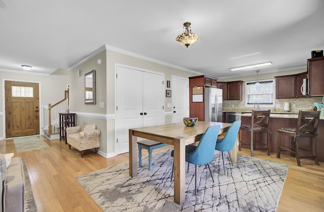 dining room with light wood-style floors, baseboards, stairs, and ornamental molding