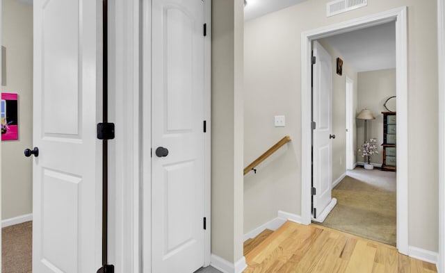 hallway featuring baseboards, an upstairs landing, visible vents, and light wood-style floors