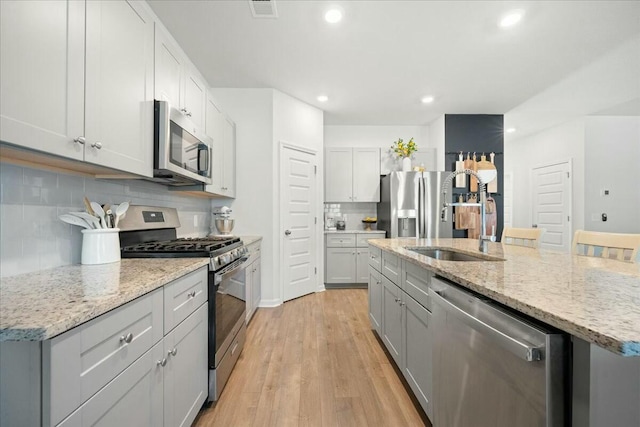 kitchen with stainless steel appliances, visible vents, light wood-style flooring, a sink, and an island with sink