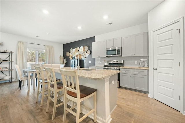 kitchen with a breakfast bar area, tasteful backsplash, visible vents, appliances with stainless steel finishes, and light wood-style floors