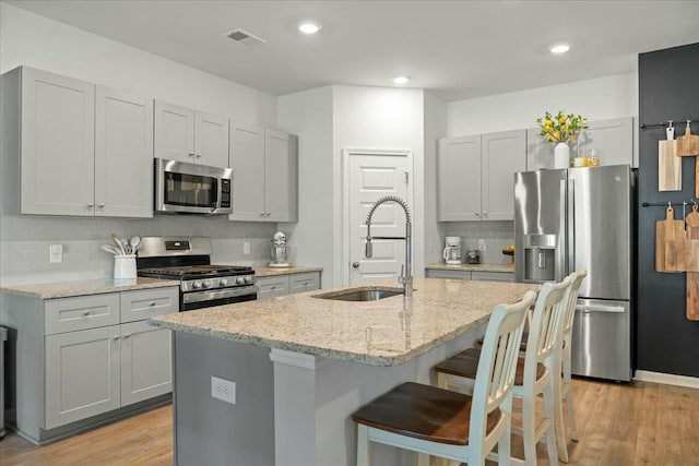 kitchen featuring appliances with stainless steel finishes, a sink, light stone countertops, and decorative backsplash