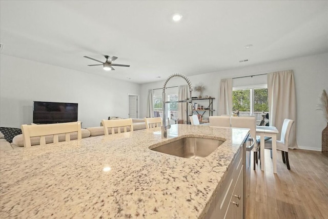 kitchen with ceiling fan, a sink, open floor plan, light stone countertops, and light wood finished floors