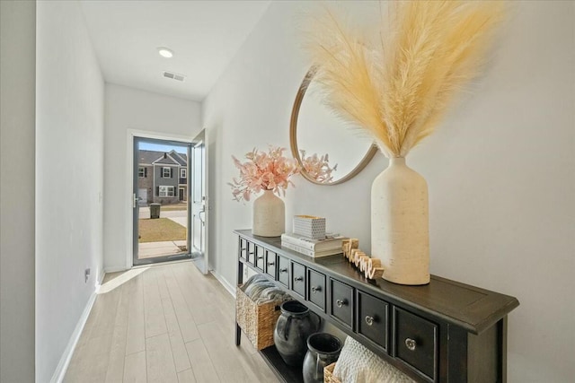 hallway with baseboards, visible vents, and wood finished floors