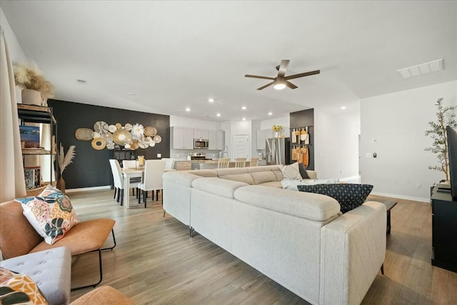 living room featuring recessed lighting, a ceiling fan, visible vents, baseboards, and light wood finished floors