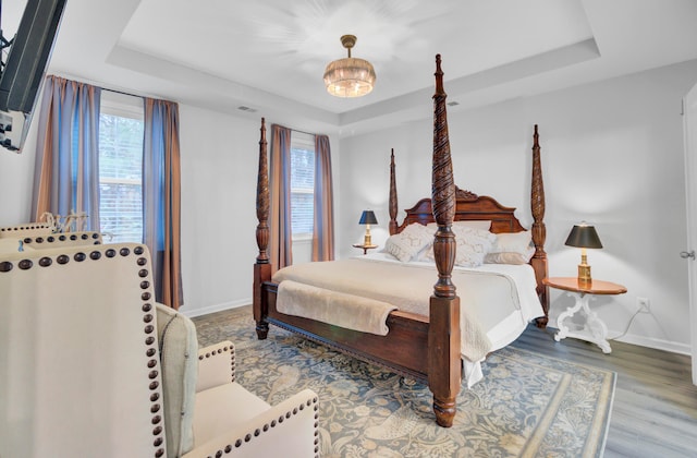 bedroom with hardwood / wood-style flooring, a chandelier, and a tray ceiling