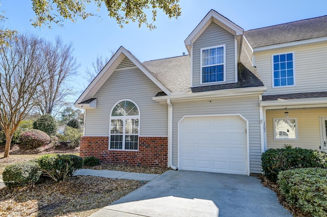 view of front facade with an attached garage, driveway, brick siding, and a shingled roof