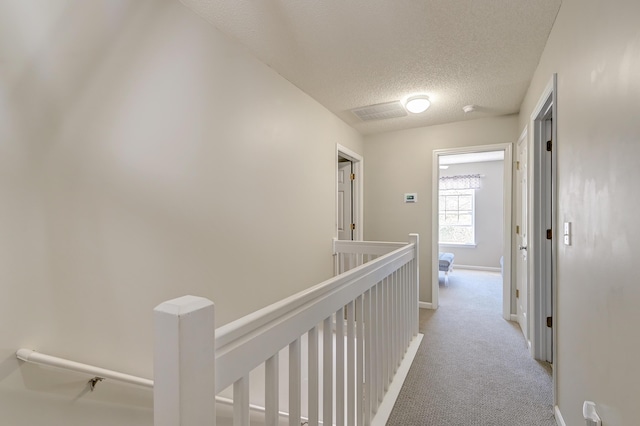 hallway with light carpet, a textured ceiling, an upstairs landing, and baseboards