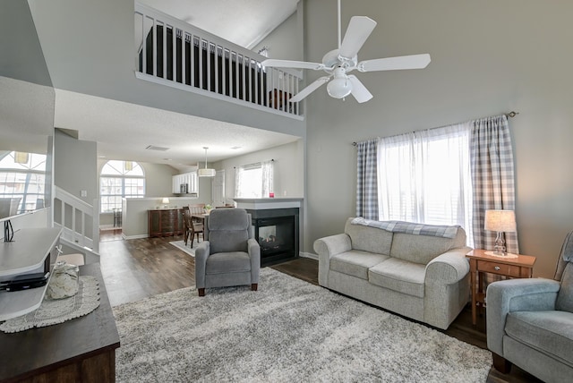 living area with baseboards, ceiling fan, wood finished floors, a high ceiling, and a multi sided fireplace