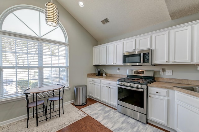 kitchen with lofted ceiling, stainless steel appliances, plenty of natural light, and white cabinetry