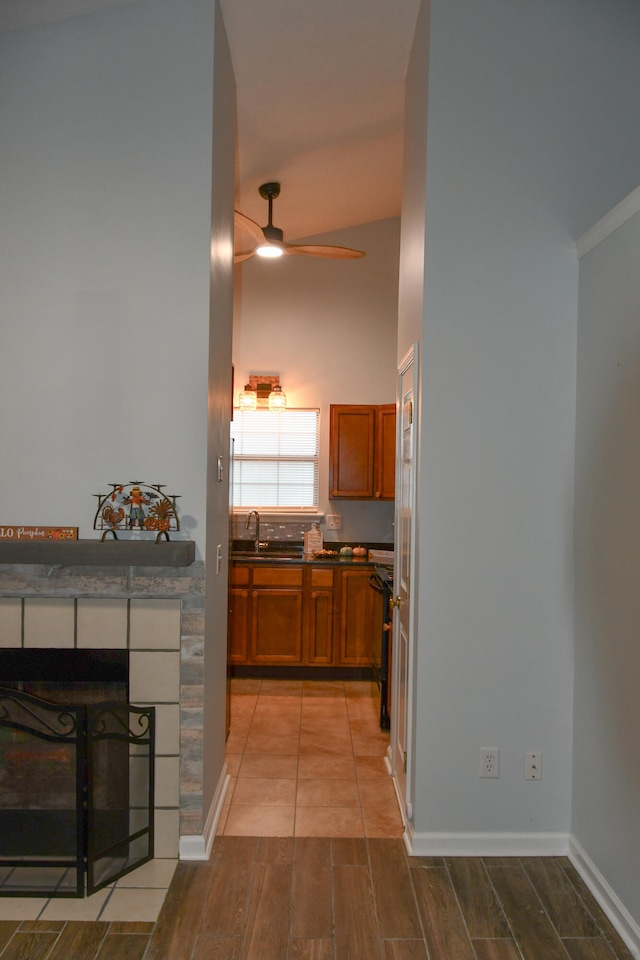 kitchen featuring ceiling fan, light hardwood / wood-style floors, a tiled fireplace, and lofted ceiling