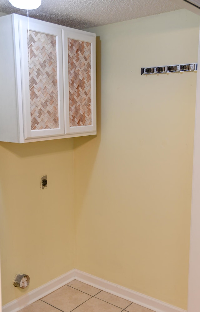 laundry room featuring cabinets, a textured ceiling, light tile patterned floors, and electric dryer hookup