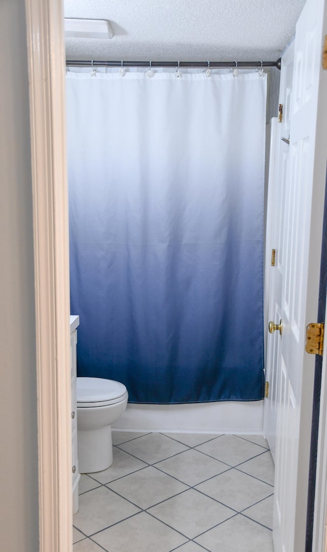 bathroom featuring a shower with curtain, tile patterned floors, toilet, and a textured ceiling