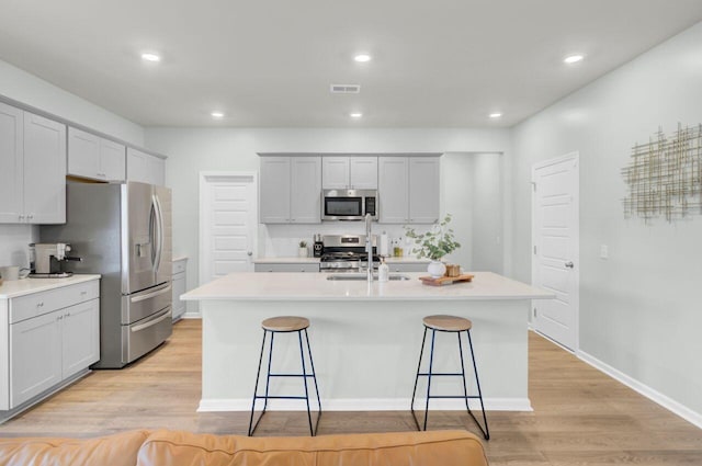 kitchen featuring a center island with sink, light wood finished floors, visible vents, appliances with stainless steel finishes, and a kitchen bar