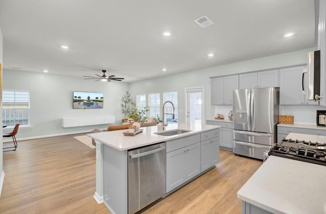 kitchen with stainless steel appliances, light countertops, visible vents, a sink, and an island with sink