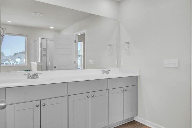 full bathroom with double vanity, wood finished floors, a sink, and baseboards