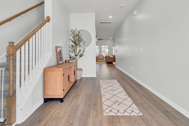 hallway featuring baseboards, stairs, visible vents, and wood finished floors