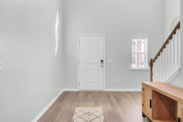 foyer entrance featuring baseboards, a high ceiling, stairway, and light wood-style floors