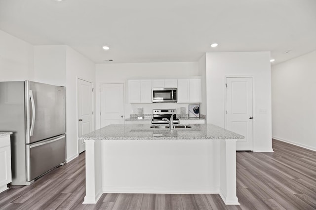 kitchen featuring light stone countertops, appliances with stainless steel finishes, white cabinetry, an island with sink, and wood finished floors