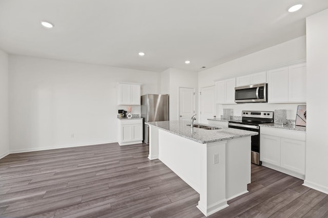 kitchen with a center island with sink, stainless steel appliances, white cabinets, a sink, and wood finished floors