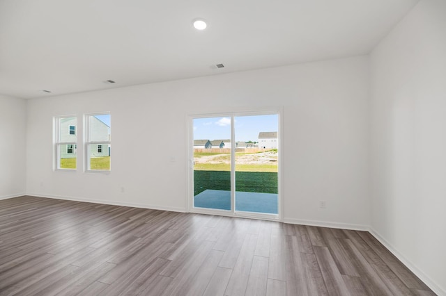 empty room featuring a healthy amount of sunlight, visible vents, and wood finished floors