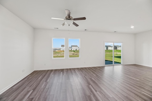 spare room with a ceiling fan, visible vents, baseboards, and dark wood-type flooring