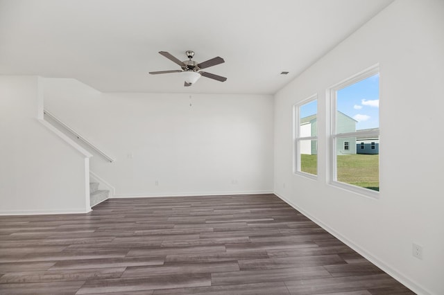 spare room featuring stairs, dark wood-style flooring, a ceiling fan, and baseboards