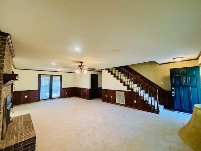 living room with french doors, carpet floors, a brick fireplace, wooden walls, and ornamental molding