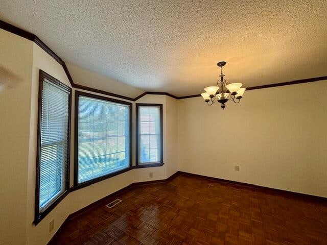 spare room featuring dark parquet flooring, an inviting chandelier, a textured ceiling, and crown molding