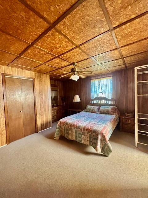 carpeted bedroom featuring a closet, ceiling fan, and wood walls