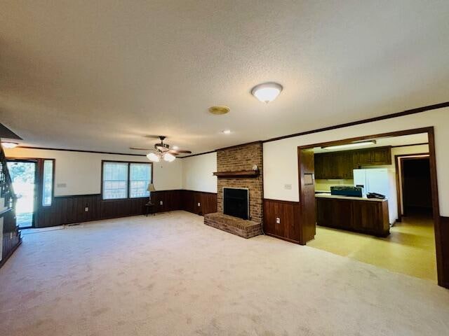 unfurnished living room featuring light carpet, ceiling fan, a textured ceiling, ornamental molding, and a fireplace