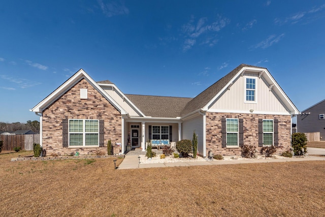 craftsman-style house with stone siding, a front lawn, and fence