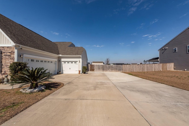 view of home's exterior with an attached garage, board and batten siding, fence, stone siding, and driveway