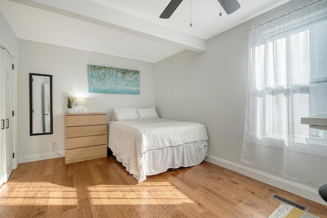 bedroom with ceiling fan, beam ceiling, and wood-type flooring