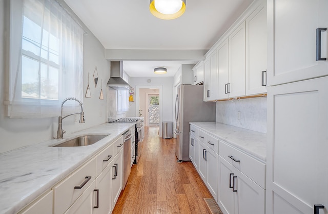 kitchen with white cabinets, sink, light hardwood / wood-style flooring, wall chimney exhaust hood, and light stone counters