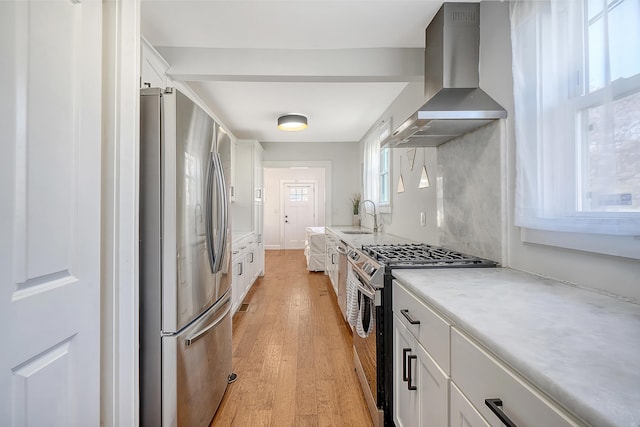 kitchen with wall chimney range hood, sink, appliances with stainless steel finishes, light hardwood / wood-style floors, and white cabinetry