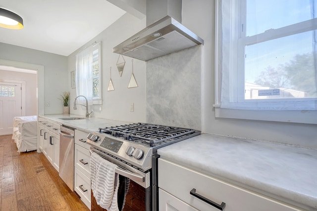 kitchen featuring stainless steel appliances, sink, wall chimney range hood, light hardwood / wood-style flooring, and white cabinetry