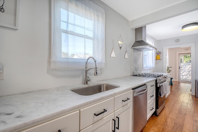 kitchen with white cabinetry, sink, wall chimney exhaust hood, stainless steel appliances, and light hardwood / wood-style floors