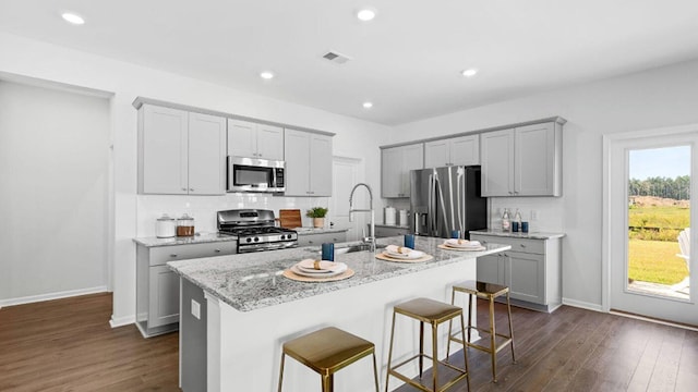 kitchen featuring visible vents, stainless steel appliances, a sink, and a center island with sink