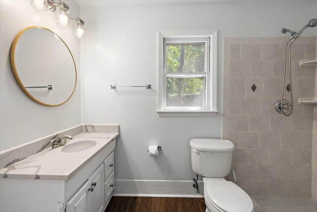 bathroom featuring toilet, a tile shower, hardwood / wood-style flooring, and vanity